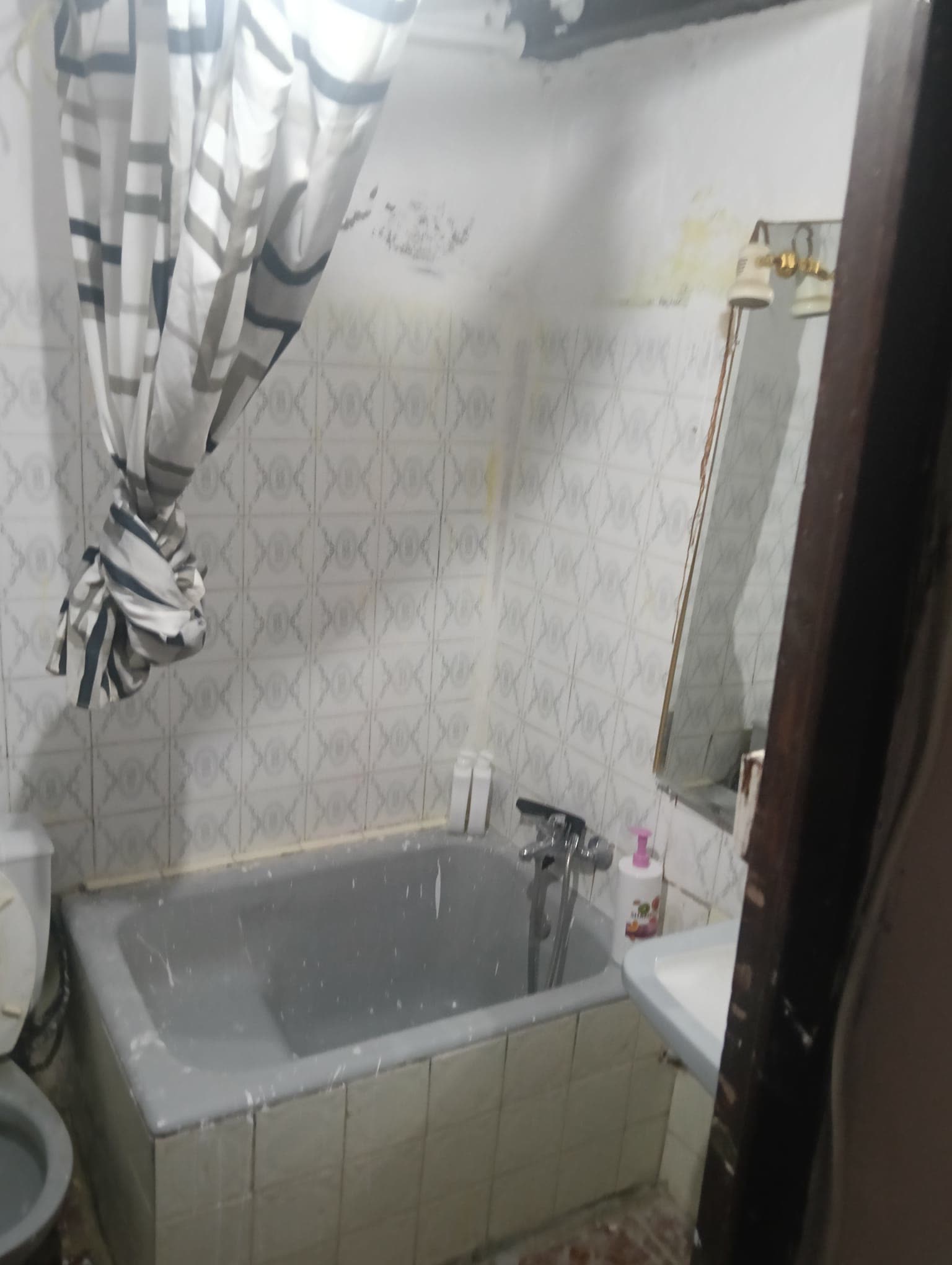 Bañera y grifería antiguas junto a un espejo con el marco oxidado