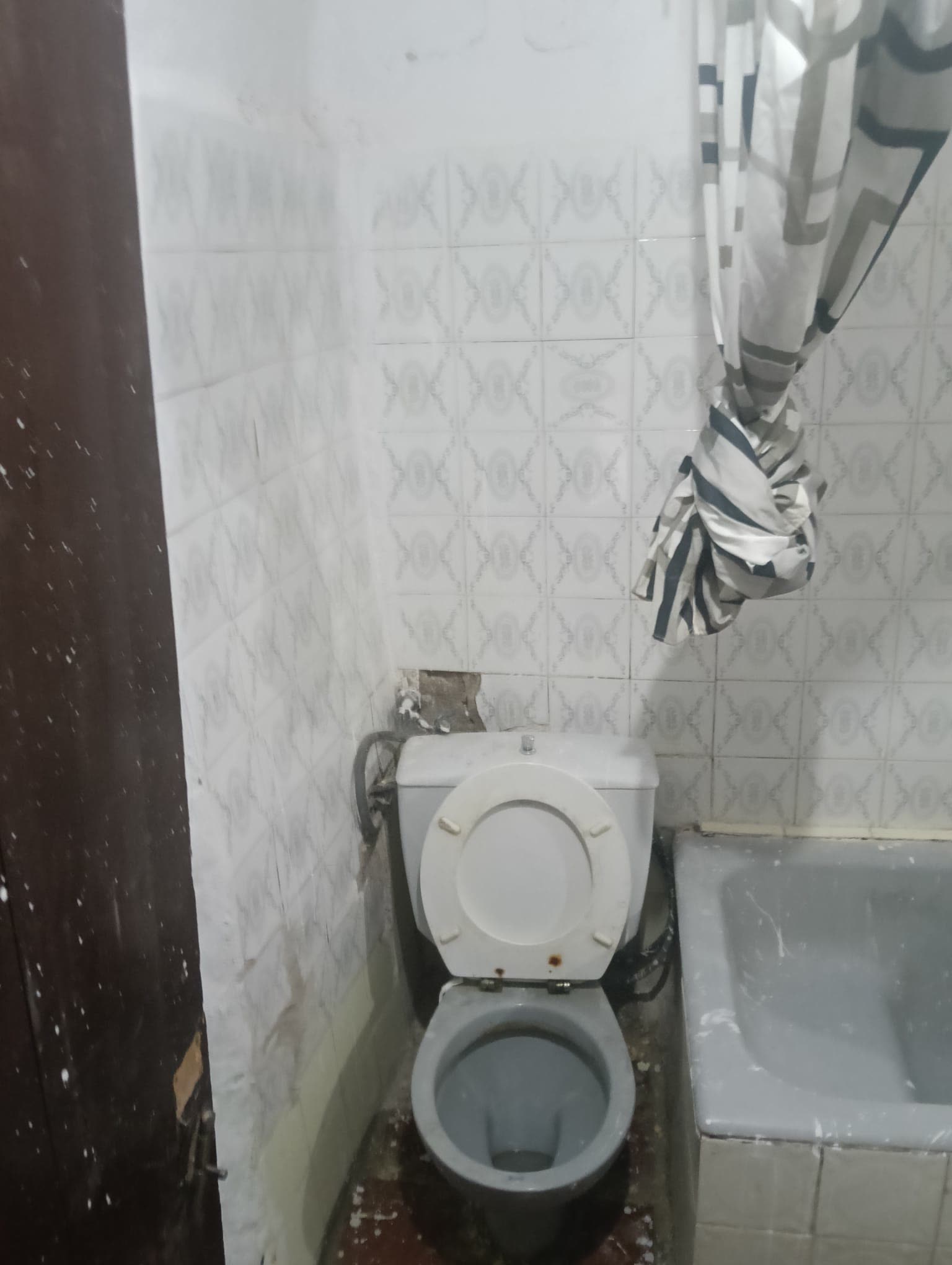 Inodoro antiguo con un hueco de azulejo roto en la pared de detrás