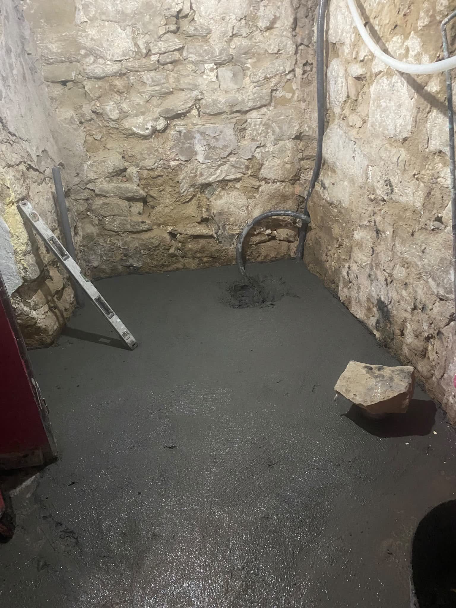 Solera de mortero recién vertida y nivelada junto a un muro de piedra visto en obra