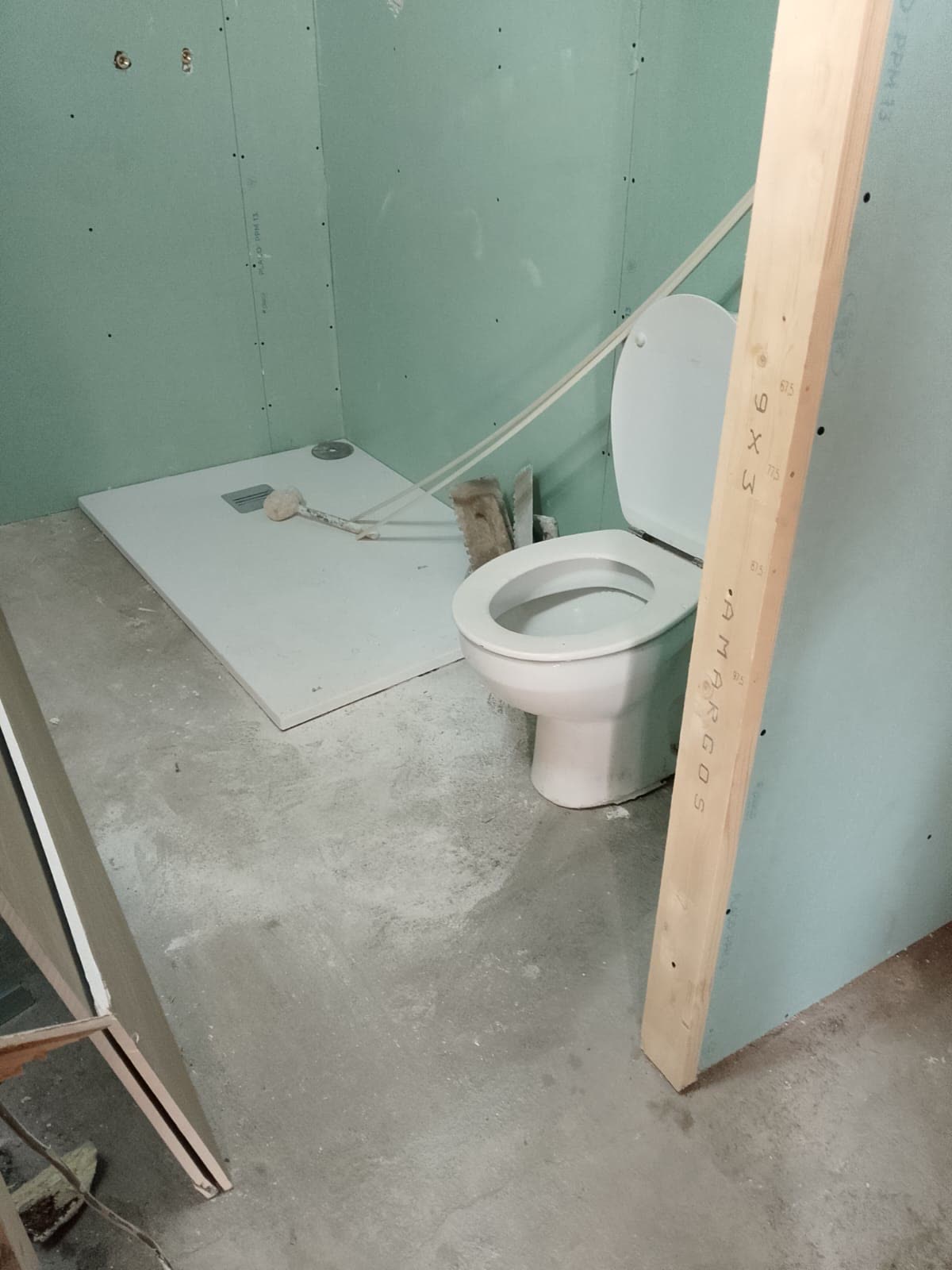 Tabique nuevo levantado junto a un plato de ducha en una obra de baño antiguo