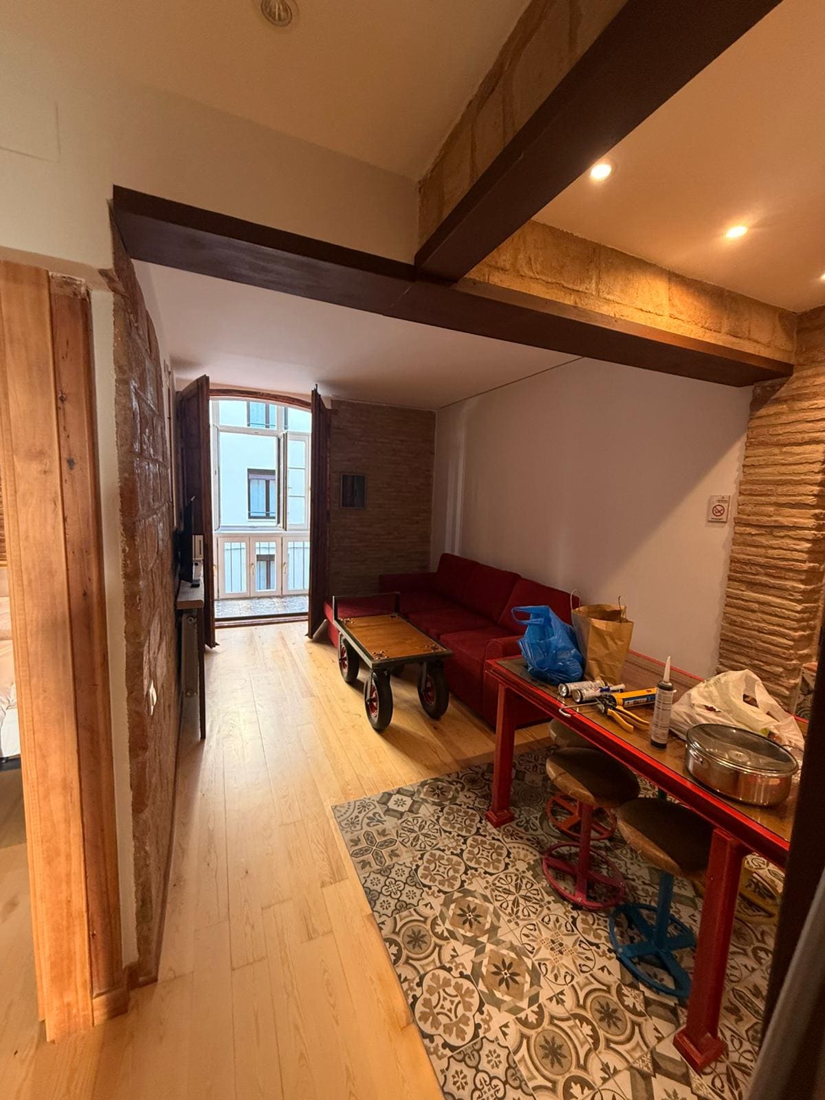Salón con pared de ladrillo visto y vigas de madera recuperadas en una reforma integral de JIMA